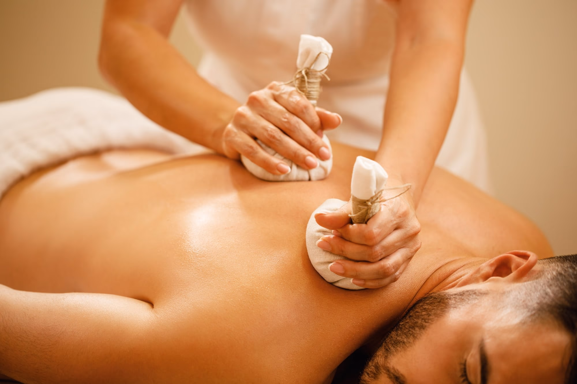 Warm herbal poultices being pressed along a person’s back during a traditional potli massage