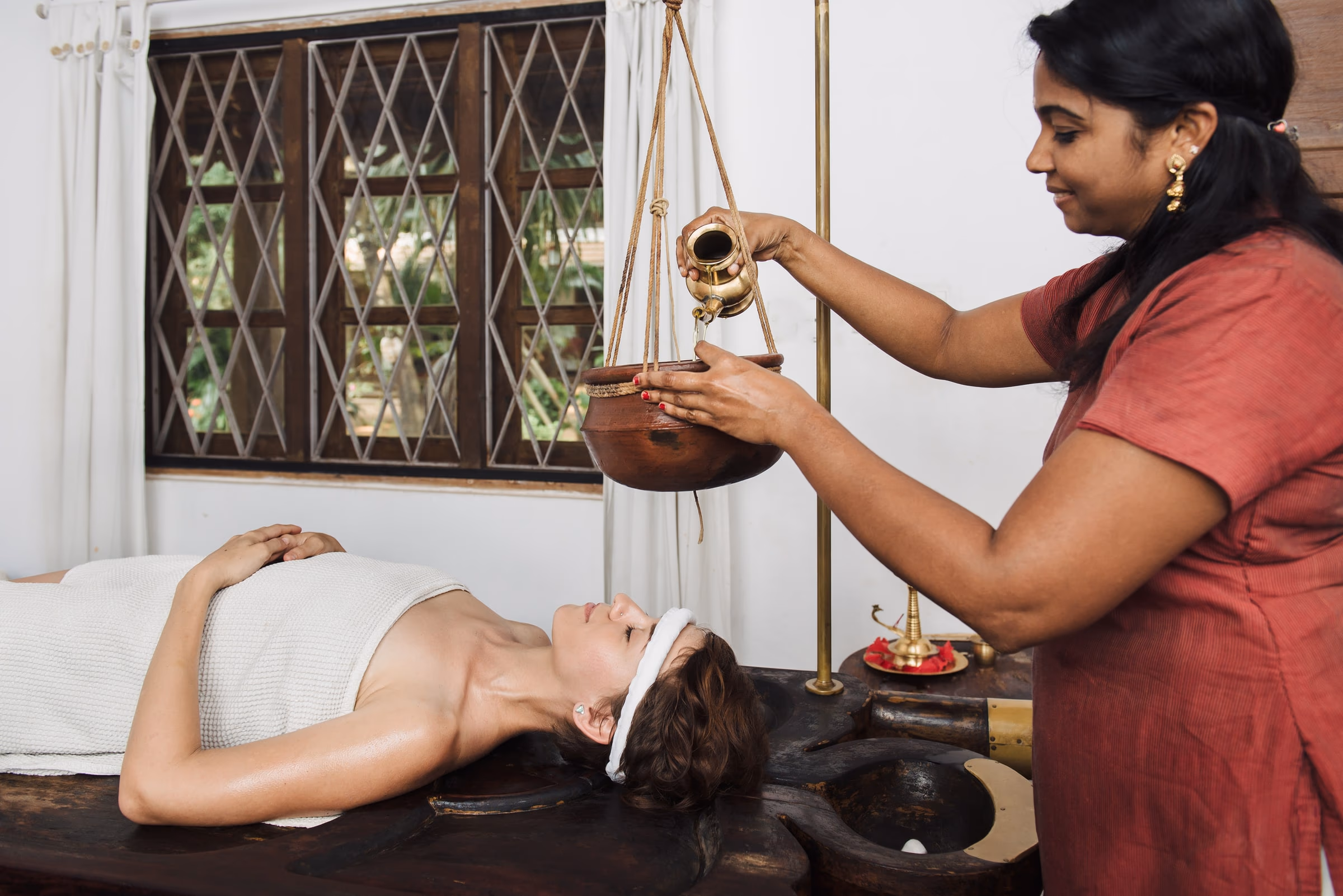 Warm herbal oil poured from a brass vessel during a traditional Ayurvedic treatment